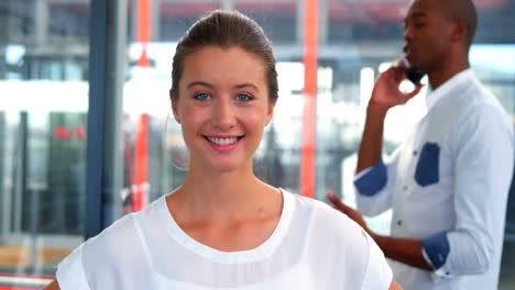 ejecutiva de negocios sonriendo a la cámara mientras un colega habla por teléfono móvil