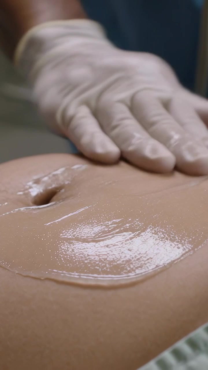 Video verticale: Clinico guantato in camice che preme, spalmando gel sull'addome sul tavolo per l'esame.