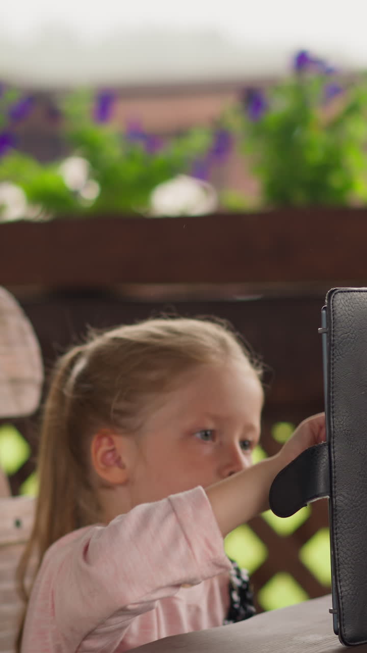 concentrada niña juega juego en línea por computadora tablet esperando mientras la lluvia se detiene en la mesa de madera en la cafetería en el hotel eco cámara lenta