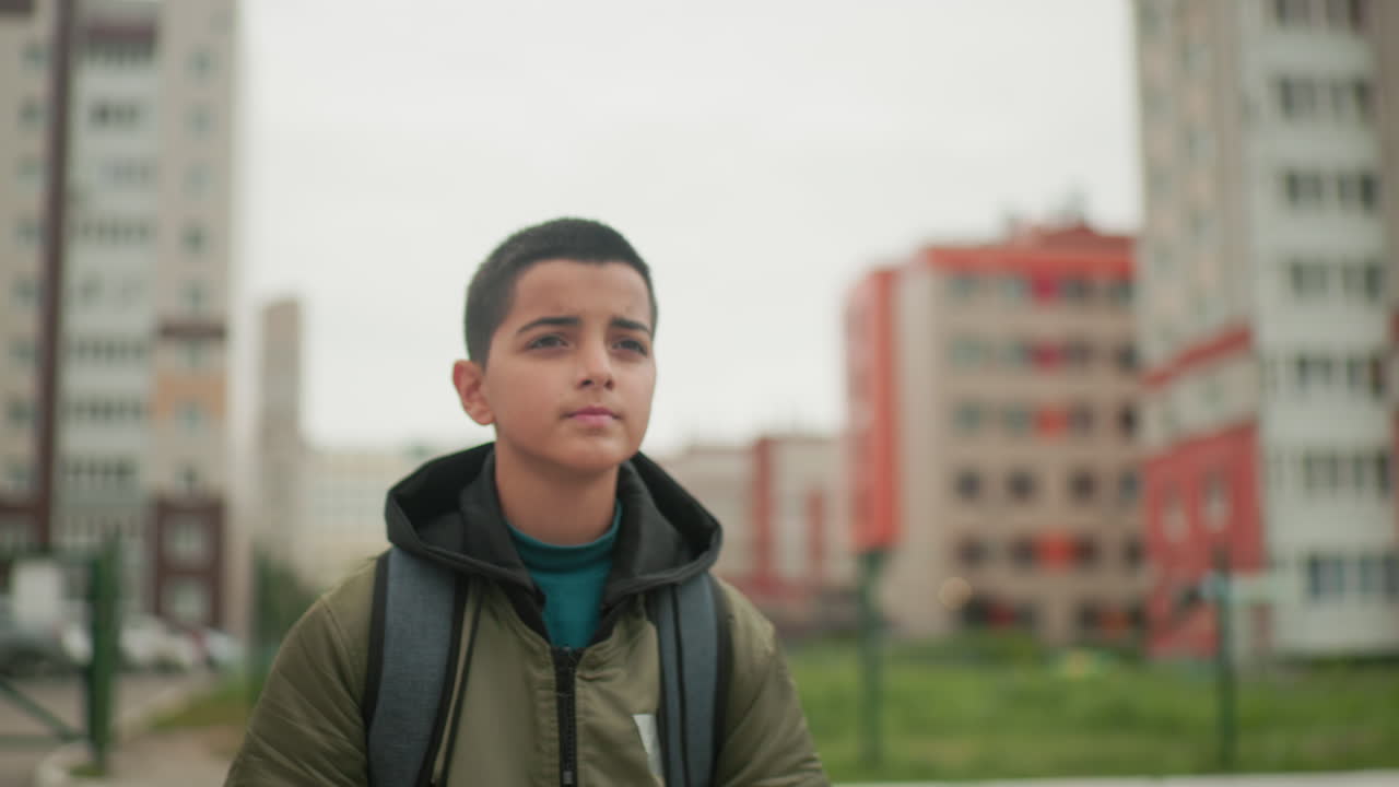 Primer plano de un niño corriendo al aire libre con una mochila, con un edificio residencial borroso de fondo que muestra energía en movimiento, determinación y estilo de vida urbano, representando la rutina escolar