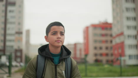 close up of young boy running outdoors wearing backpack with blurred residential building background showing motion energy determination and urban lifestyle representing school routine