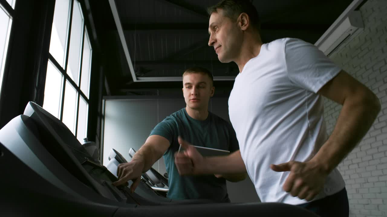 hombre haciendo ejercicio en la cinta de correr con un joven entrenador
