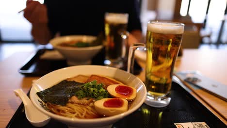 two people sharing ramen and beer at a table.