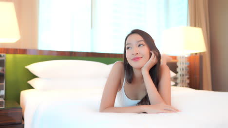 an asian woman comfortably lying on a bed in her room and watching tv, slow motion, face close-up