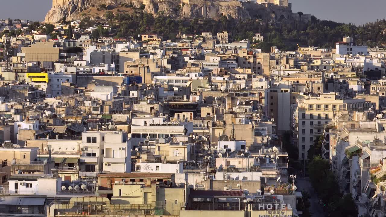 UHD 4K drone view of the Acropolis and Parthenon in Athens, Greece at golden hour. Ancient ruins rise above the dense modern cityscape. Iconic UNESCO World Heritage site from aerial perspective.