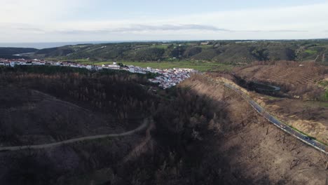 drone flyover burnt forest area by small village in algarve, flying backward