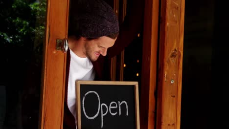 owner leaning at door with open sign board in cafe