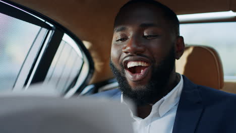 Retrato-De-Un-Alegre-Hombre-De-Negocios-Africano-Mirando-Documentos-Financieros-En-El-Coche.