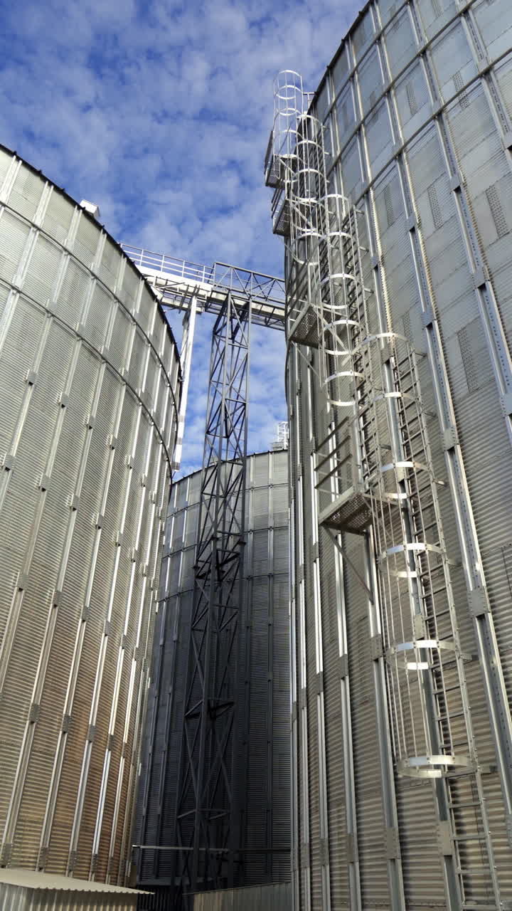 Aluminum grain elevators. Agricultural equipment for storing harvest. Modern warehouse. Granary in a sunny day. Close-up. Vertical video