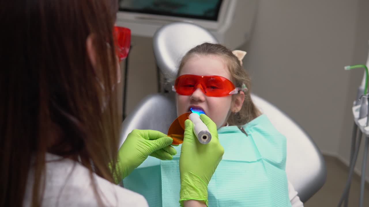 menina bonita na clínica do dentista recebe tratamento dental para preencher uma cavidade em um dente. restauração dental e polimerização de material com luz uv. filmado em 4k