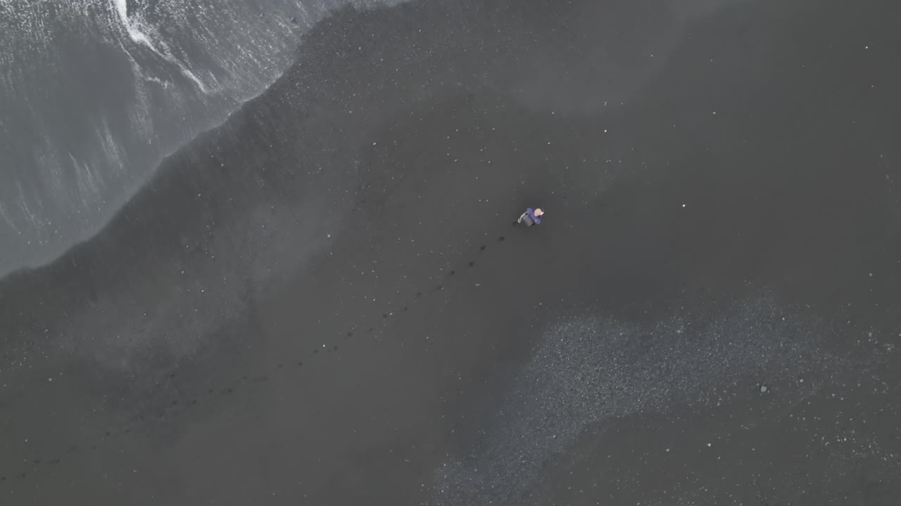 Person Walking on a Black Sand Beach with Waves