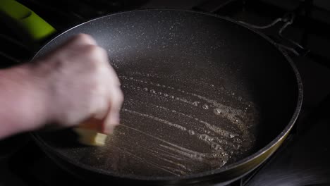 greasing hot cast iron pan with butter before pouring eggs for frying