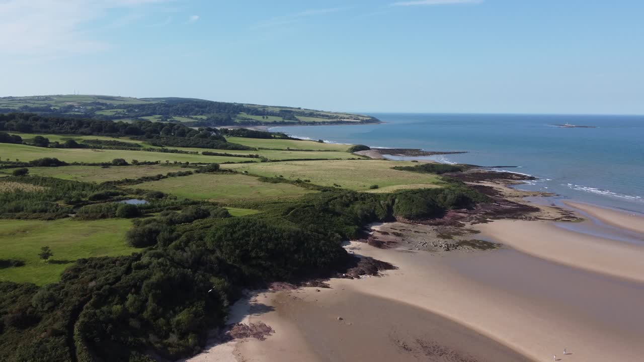 Splendido filmato cinematografico con drone sui verdi pascoli e sulla costa, con onde che si infrangono sulla costa orientale dell'Anglesey in Galles, Regno Unito.