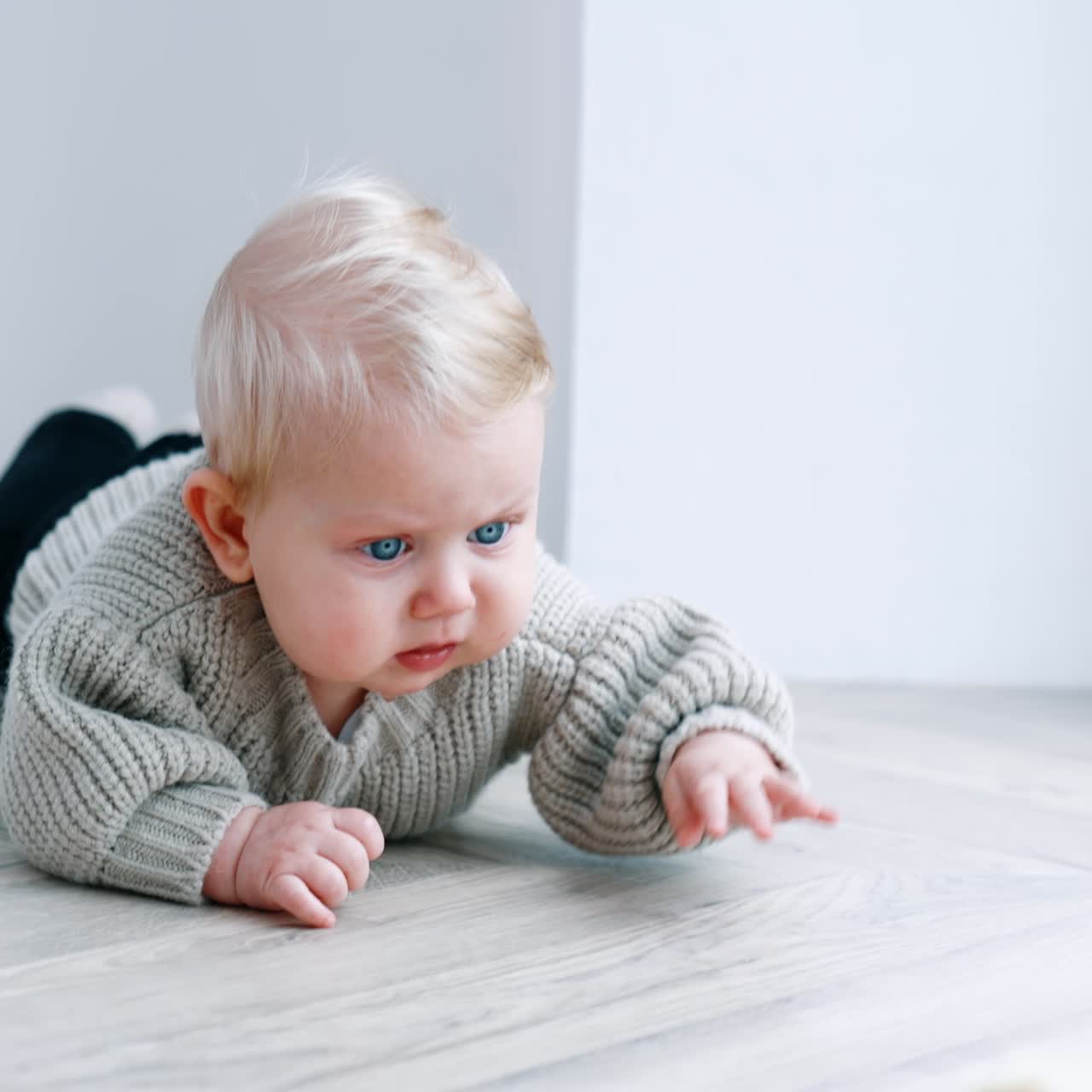 Adorabile neonato biondo con gli occhi azzurri che indossa un maglione grigio, sdraiato sulla pancia. Un bambino piccolo vicino alla finestra.