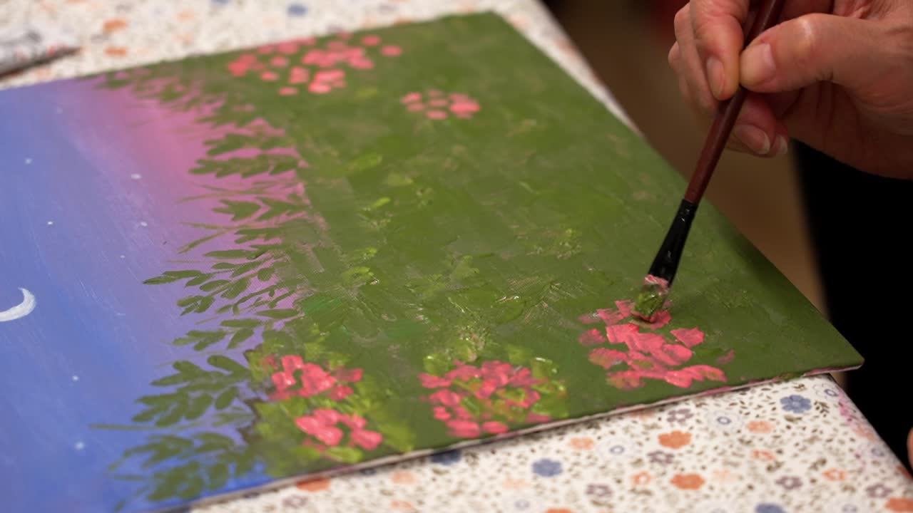 Adding pink flowers to greenery on a painted canvas