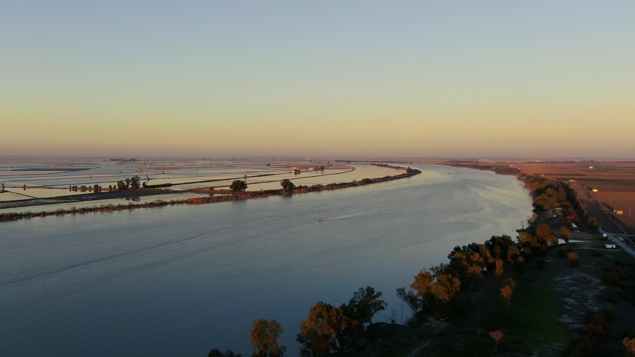 imágenes de drones de una puesta de sol sobre el río guadalquivir y sus paisajes agrícolas circundantes, con el sol en el fondo