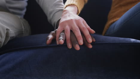 Hands-of-diverse-couple-sitting-on-sofa-in-home