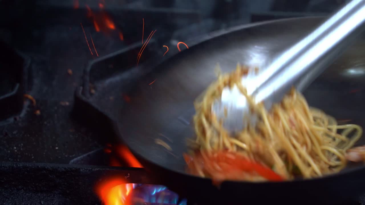 Close-up shot captures skilled chef expertly cooking stir-fry spaghetti, deftly flipping and stirring ingredients in a sizzling pan, aromatic smoke fills the atmosphere of a commercial kitchen