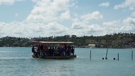 Toma-Panorámica-Derecha-De-Un-Barco-De-Transporte-Muy-Completo-Lleno-De-Lugareños-Y-Turistas-Que-Salen-De-La-Playa-De-Restinga-Navegando-Hacia-La-Playa-Barra-De-Cunhaú-En-Canguaretama-En-Rio-Grande-Do-Norte,-Brasil