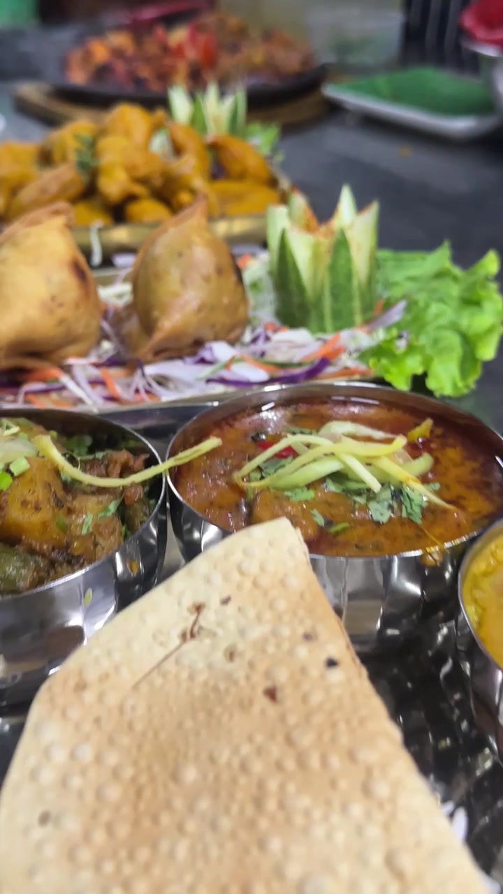 Panoramica verticale ravvicinata su pollo tandoori, pakora e samosa su un bancone in acciaio inossidabile.