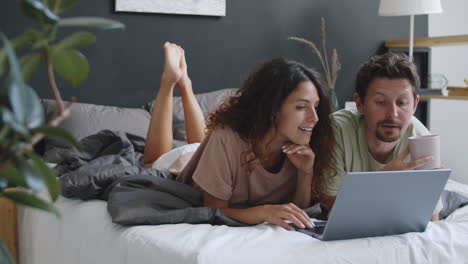pareja relajándose en la cama con una computadora portátil