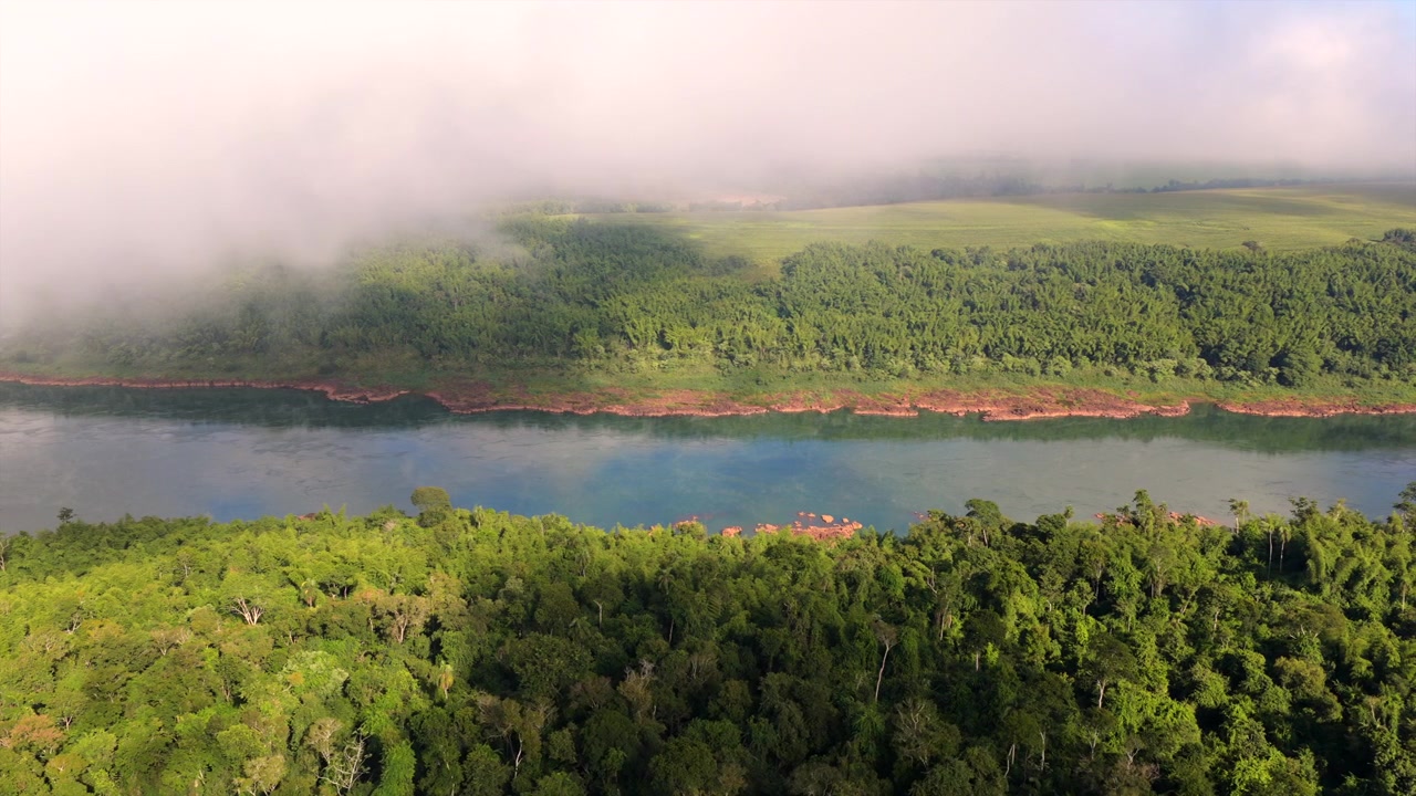 Sinuous Paraná River under low atmospheric clouds and bright afternoon sun. Right tracking, slow motion, natural landscape aerial view.