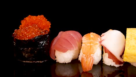 a selection of nigiri and sashimi, including shrimp, salmon, tuna, egg, squid, and roe, rotates smoothly under bright studio lighting against a black backdrop