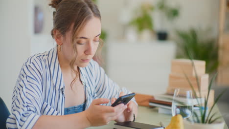 Mujer-Navegando-Por-Teléfono-Inteligente-En-El-Escritorio-De-Casa