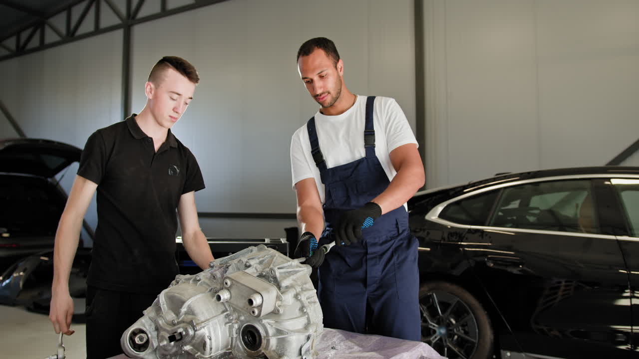 dos mecánicos trabajando en una transmisión de coche en un garaje