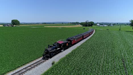 a steam train chugs along its tracks, surrounded by green fields and crops in pennsylvania on a clear summer day. scenic landscapes create a nostalgic backdrop for this classic journey.