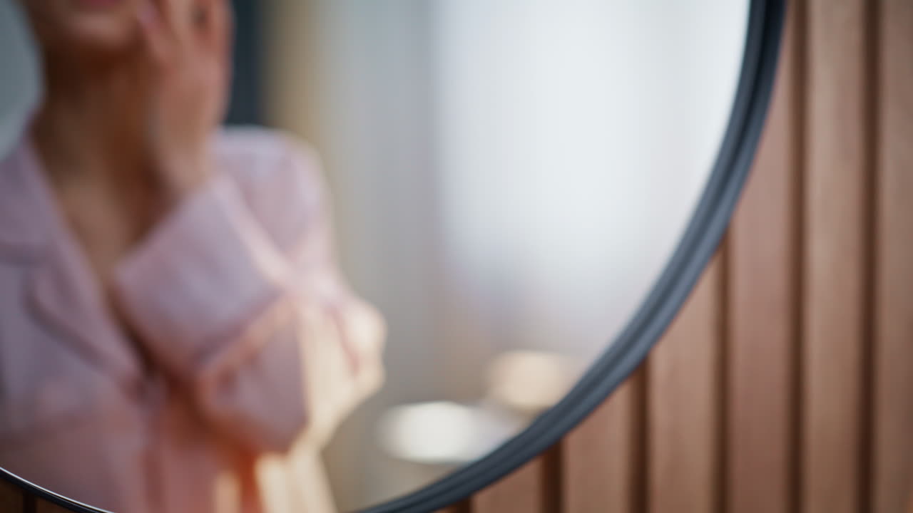 Primo piano delle mani di una donna che aprono un barattolo di crema per idratare il viso. Donna che si guarda allo specchio.