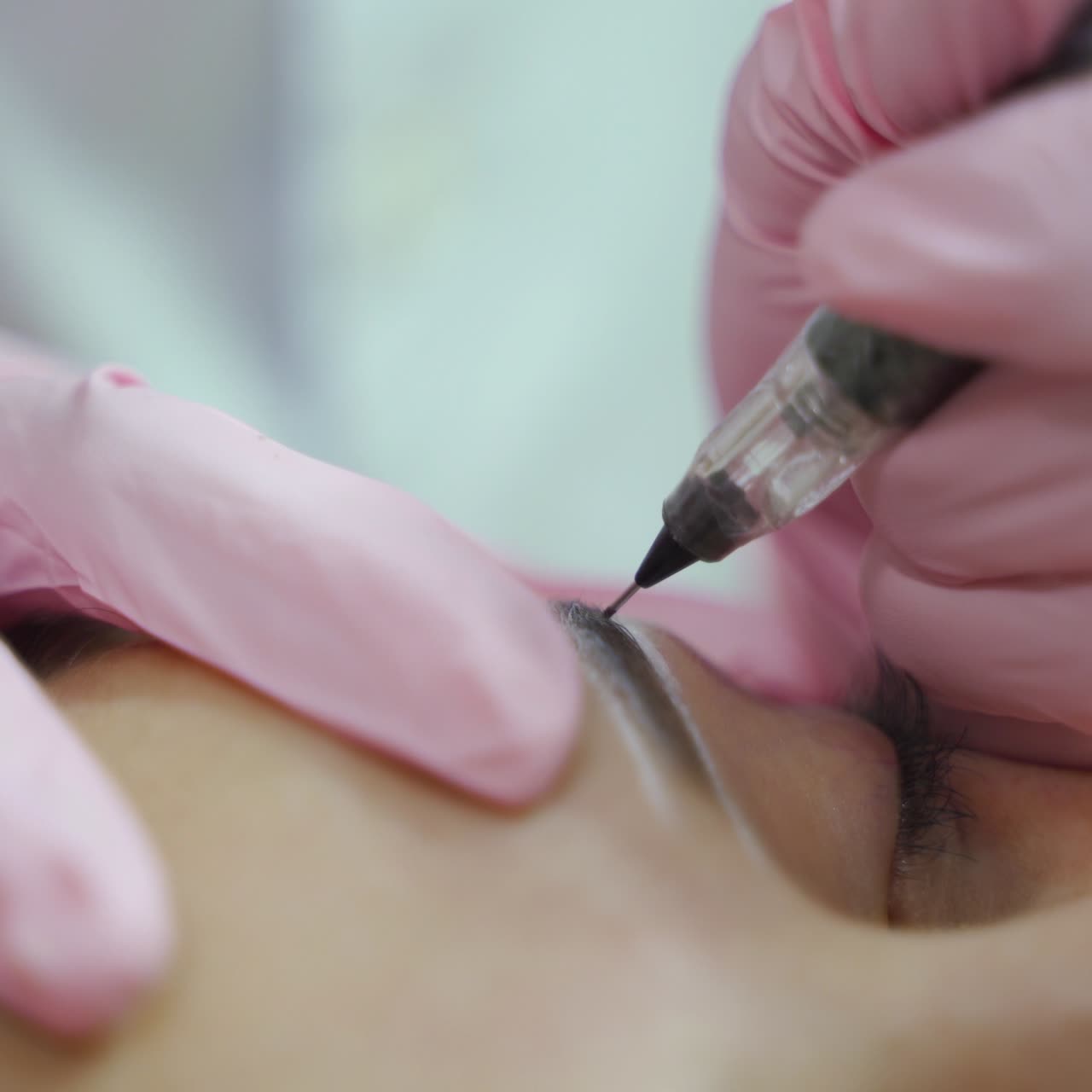 beautician in gloves is drawing the shape of the eyebrows with a special needle. The procedure of permanent makeup of eyebrows