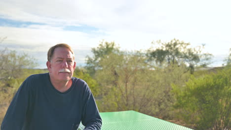 handsome man in his 60s sits alone outside in summer, enjoying nature, looks around