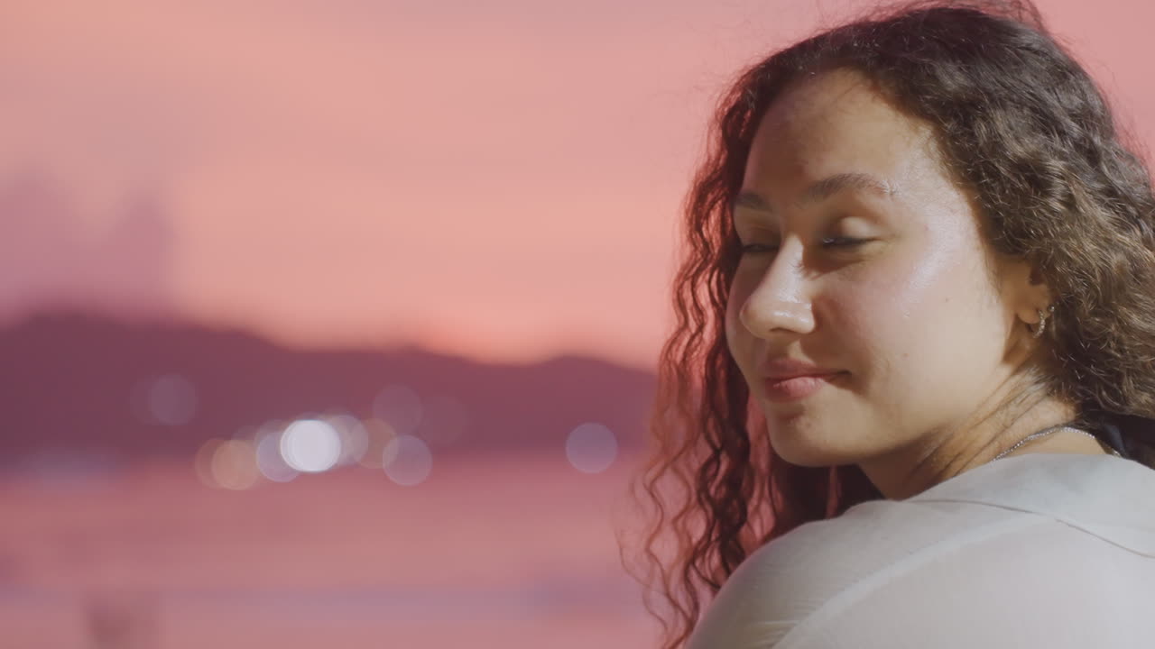 Kvindeligt portræt ved solnedgang på øens kyst, med blikket vendt mod kameraet. Blød profil, krøllet hår og et mildt smil. Kystens tusmørkelys skaber en intim og ægte portrætstemning af en eftertænksom historiefortæller på ferie.
