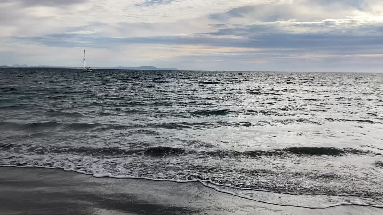 흐린 날 해변을 가로질러 명상적인 모래를 끌고 있는 잔잔한 파도의 팬