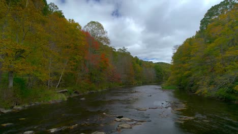 Drone-flying-above-a-river-running-through-fall-colored-mountains