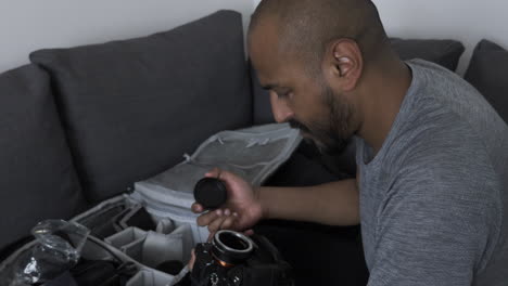 Ethnic-Minority-Adult-Male-Attaching-Lens-Adaptor-On-Camera-Indoors-On-Sofa