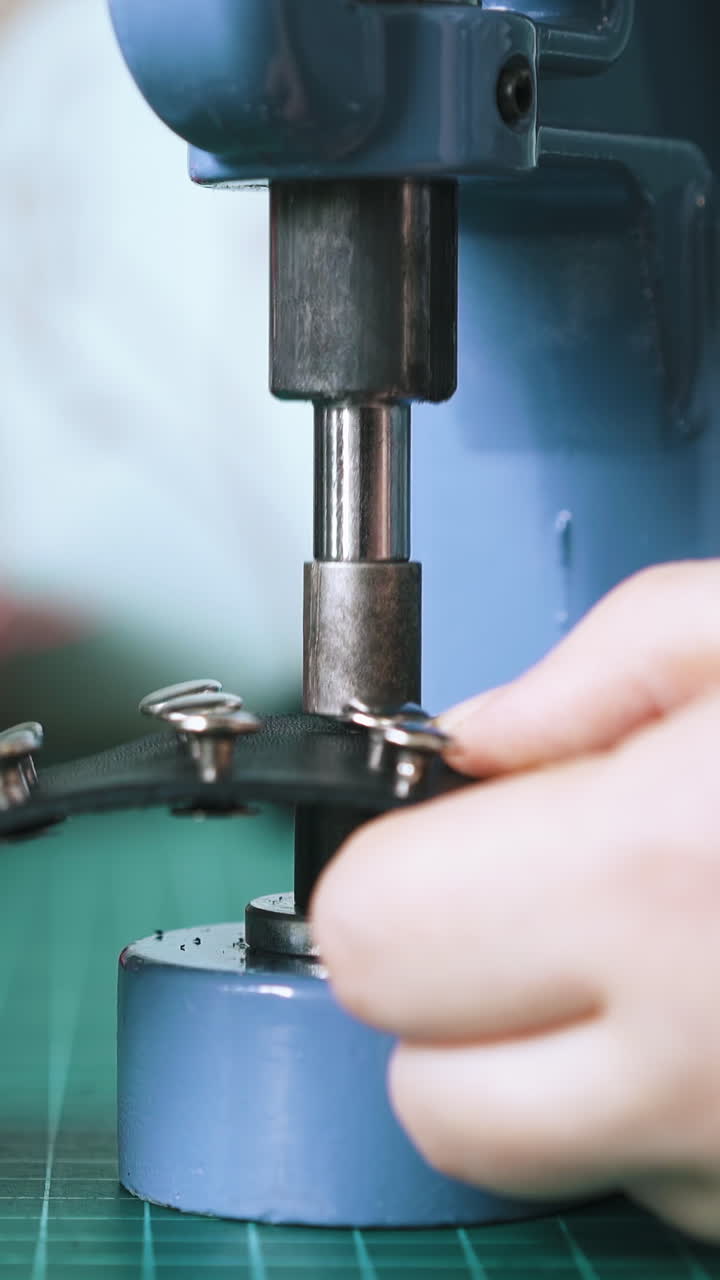 Primo piano: Designer esperta applica holnitens argentati su un girocollo di pelle nera alla moda con una pressa.