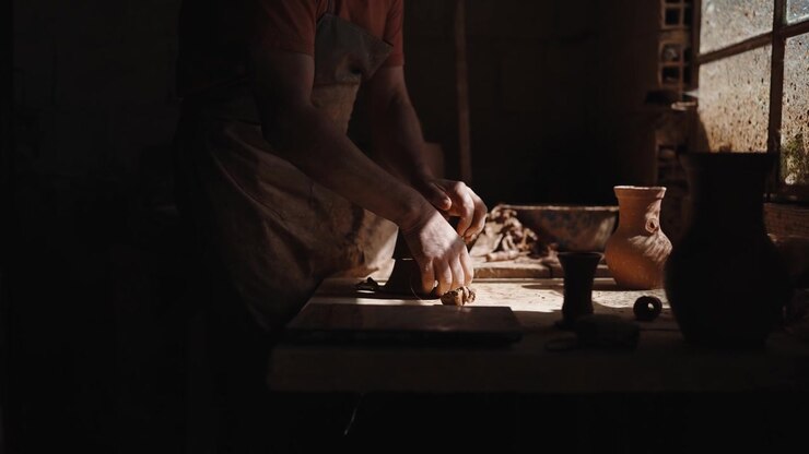 Potter working with clay, creating ceramics by hand in a dimly lit studio, emphasizing traditional craftsmanship