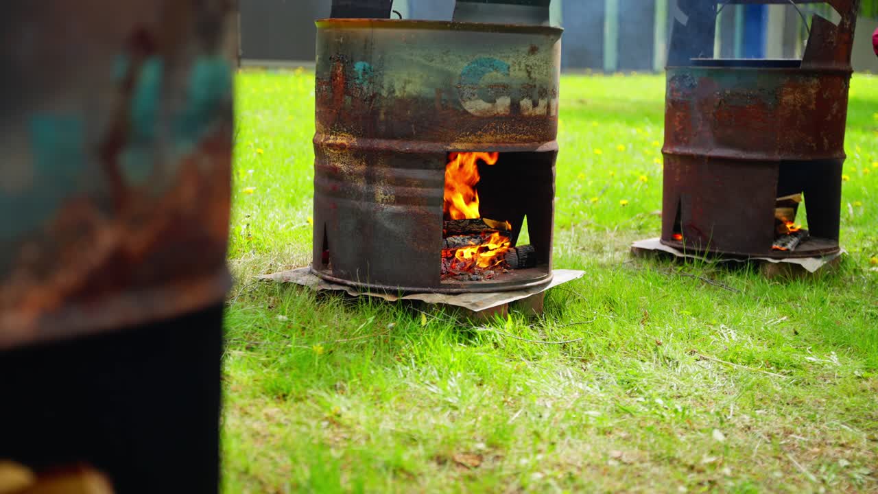 Cauldrons of soup bubble outdoors over wood fires during rustic group cookout event, slow motion