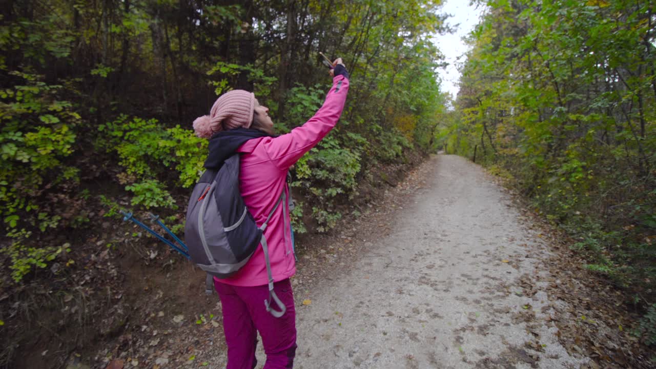 niña de senderismo con palos y mochila caminando por un camino o sendero en el bosque de montaña. tomando fotos de sí misma con su teléfono celular. viajes y estilo de vida saludable al aire libre en la temporada de otoño..