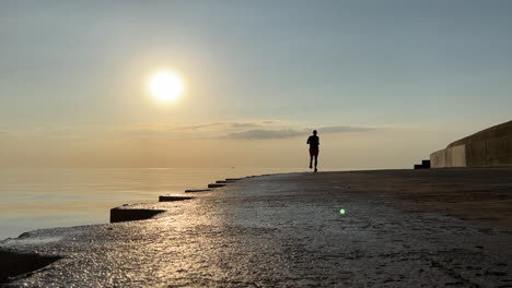 Silhouette-Eines-Läufers,-Der-Sich-Bei-Sonnenaufgang-Von-Der-Kamera-Entlang-Der-Seepromenade-Von-Chicago-Entfernt