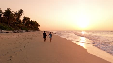 romantic aerial drone view of a couple enjoying the golden sunset on geiymiskih fannu beach in fuvahmulah, maldives.
