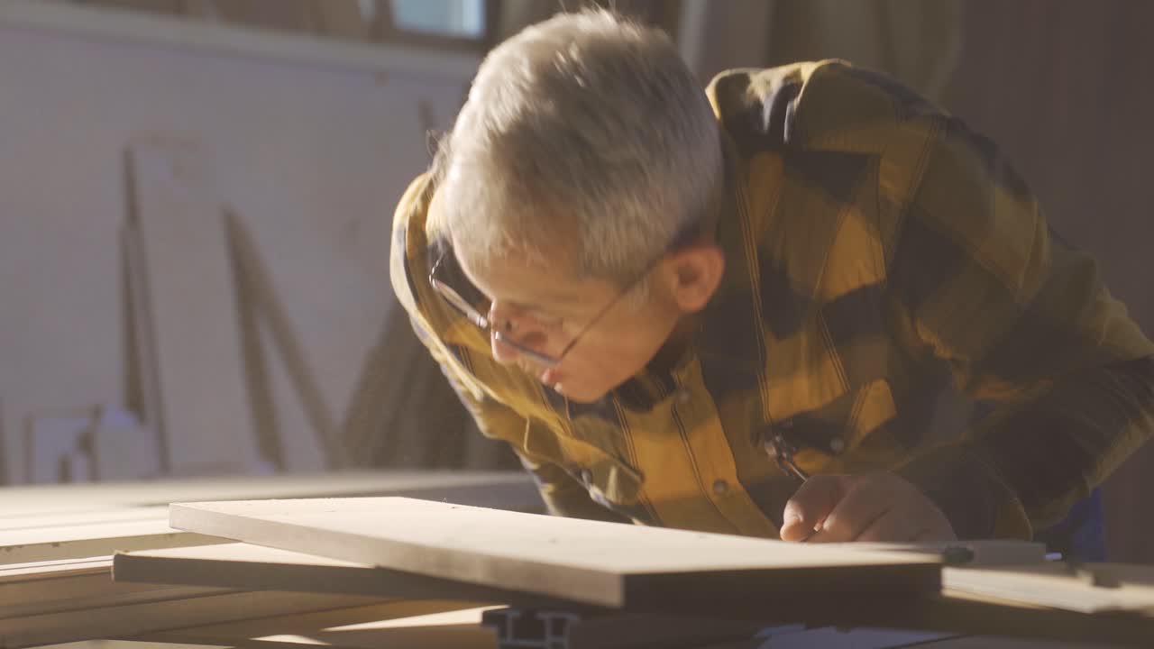 el carpintero sopla el polvo en la tabla de madera en el taller.