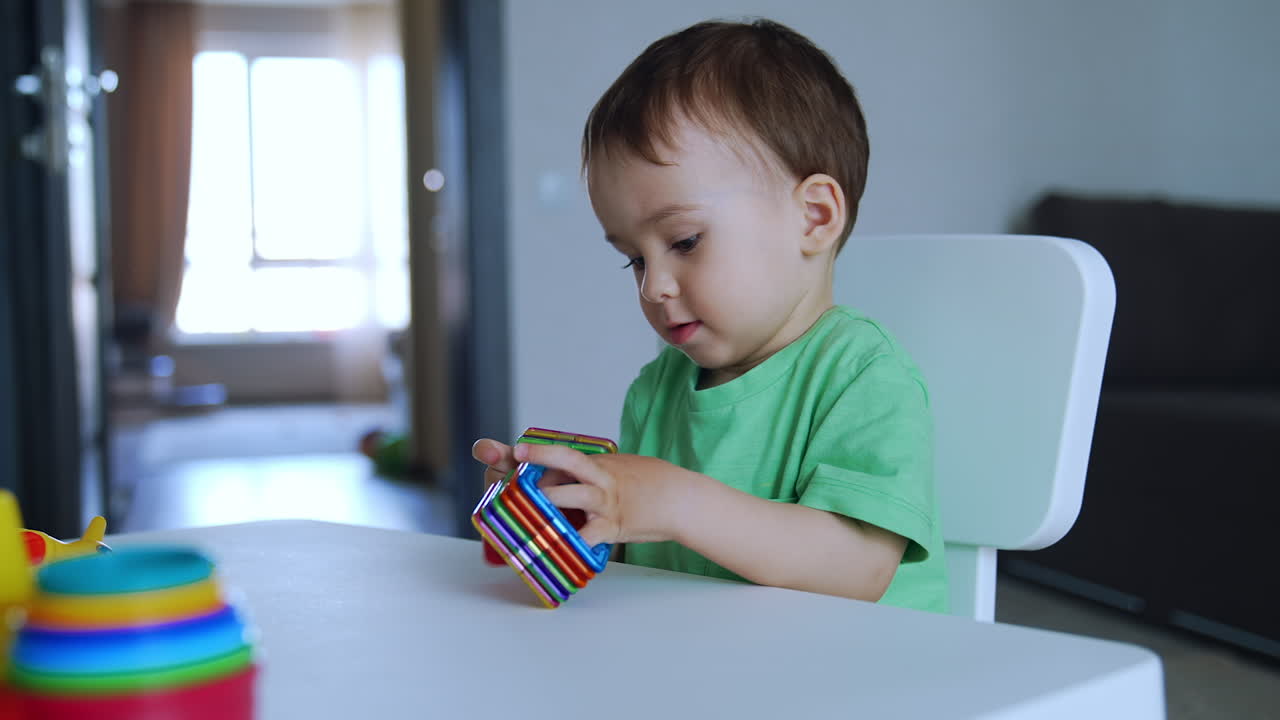 Un bambino adorabile gioca con giocattoli colorati al tavolo. Il bambino batte i giocattoli sul tavolo e li spinge.