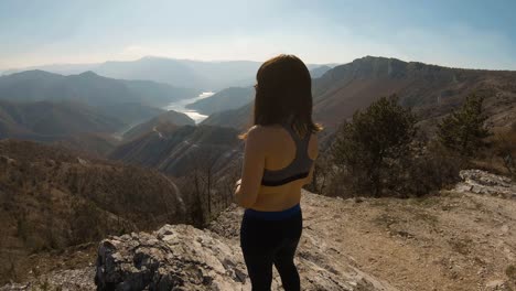 chica atleta parada en la cima de una montaña con un hermoso lago del cañón frente a ella