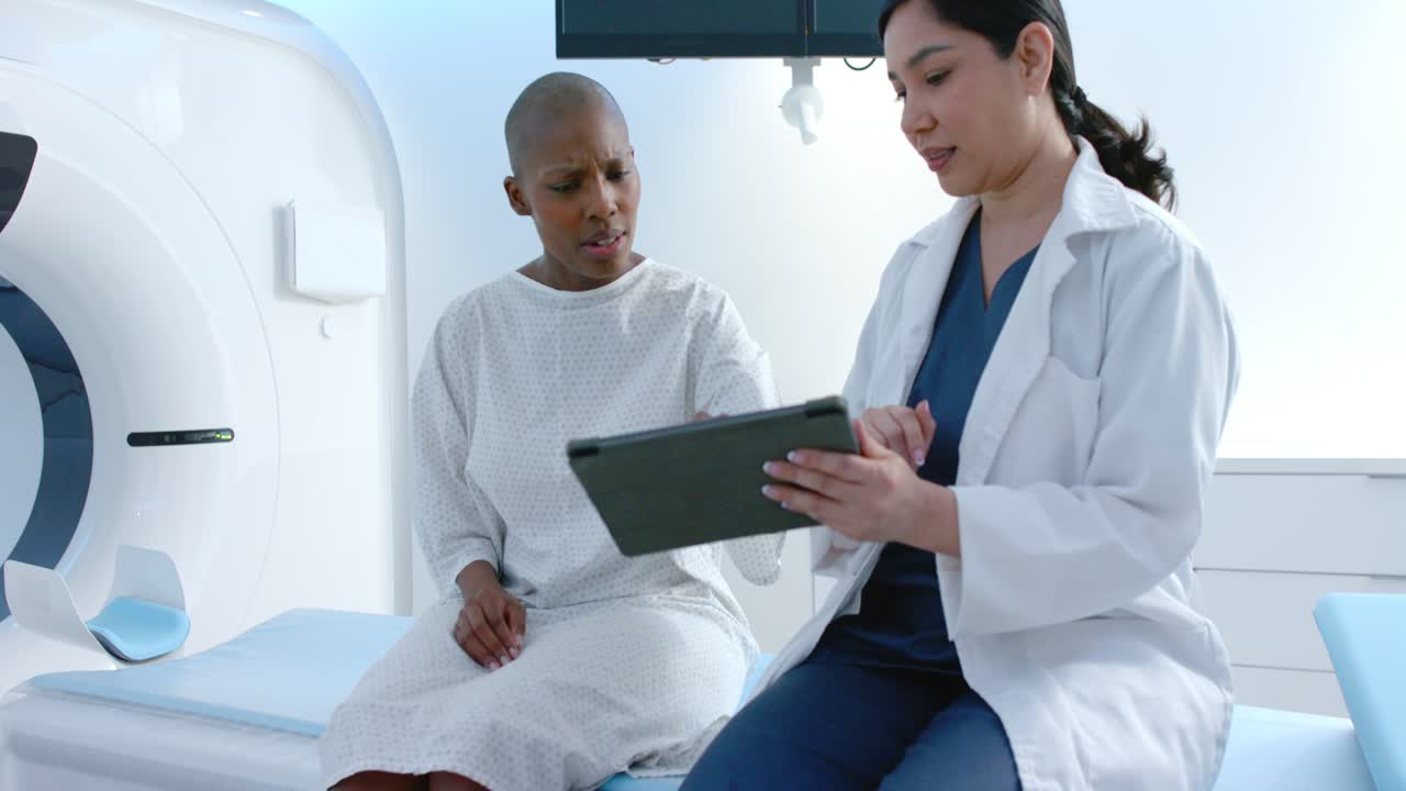 Medico asiatico che mostra una TAC su tablet a una paziente afroamericana in sala di imaging