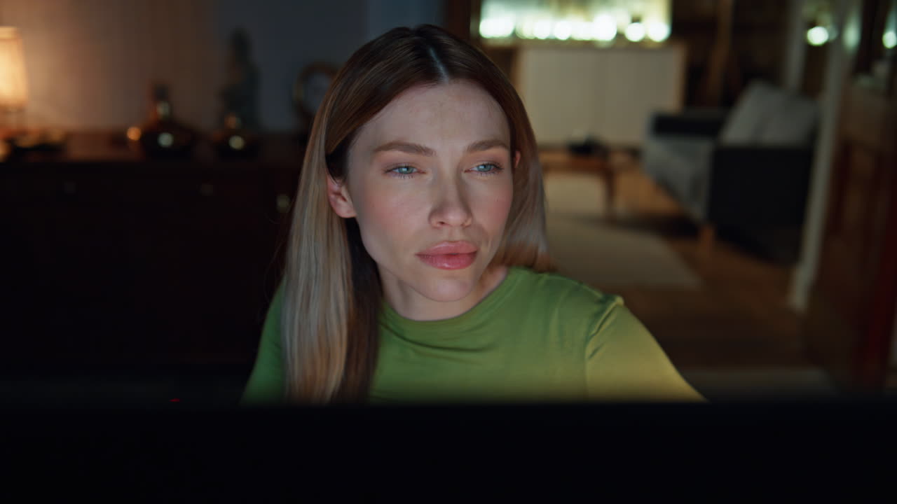 Serious woman surfing online looking computer screen at dark apartment close up.