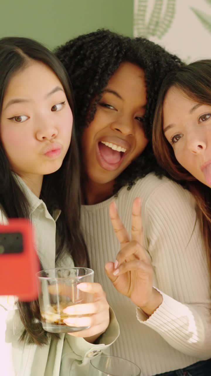 Multiracial women pulling funny faces while taking a selfie indoors