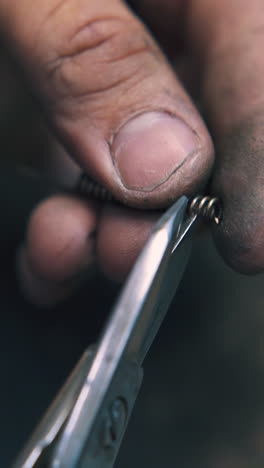 cu shot: skilled jeweler with dirty hands cuts parts from gold spiral at workplace in light craft workshop close view